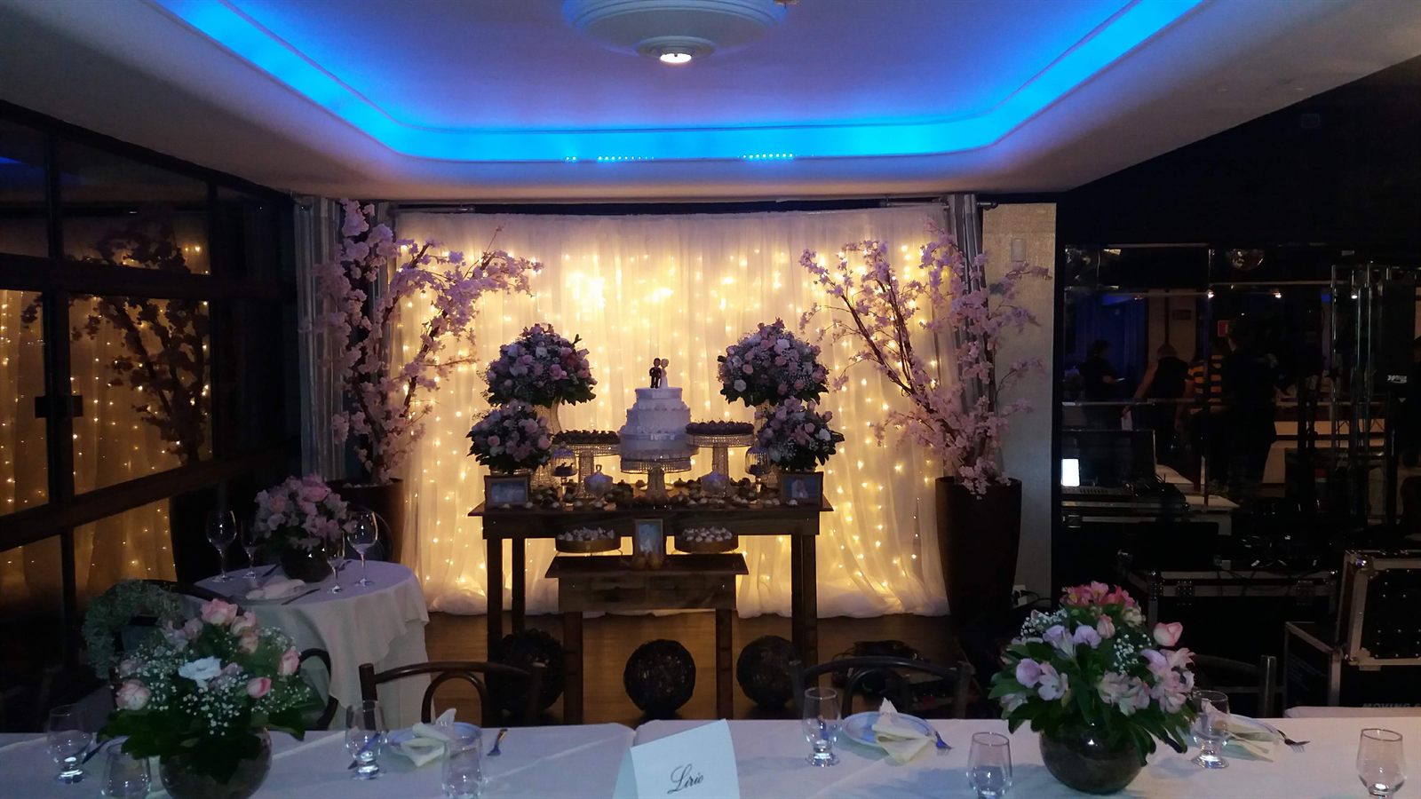 Mesa de casamento com flores, bolo e cortina de luzes
